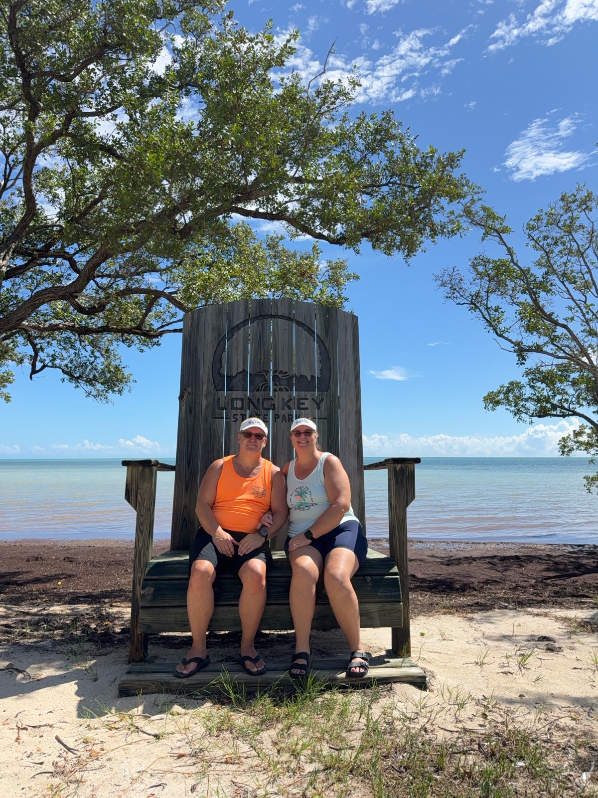 Two travelers seated together in a large wooden chair beside the water